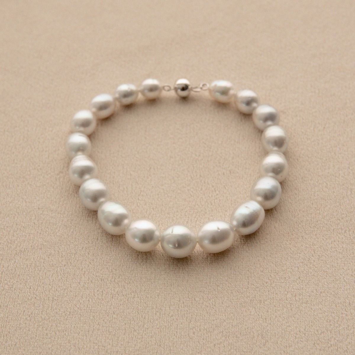 An Australian South Sea pearl strand bracelet with a 9ct white gold ball clasp, displayed on a textured beige surface.