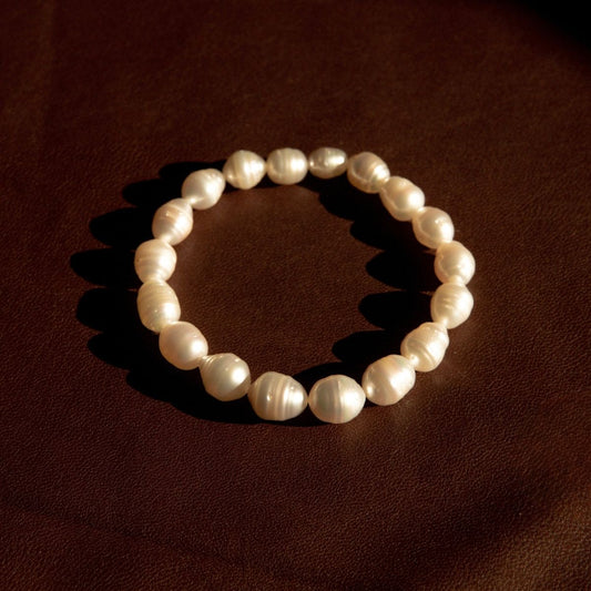 A pearl strand bracelet featuring Australian South Sea pearls, arranged in a circle on a dark brown textured surface.earl