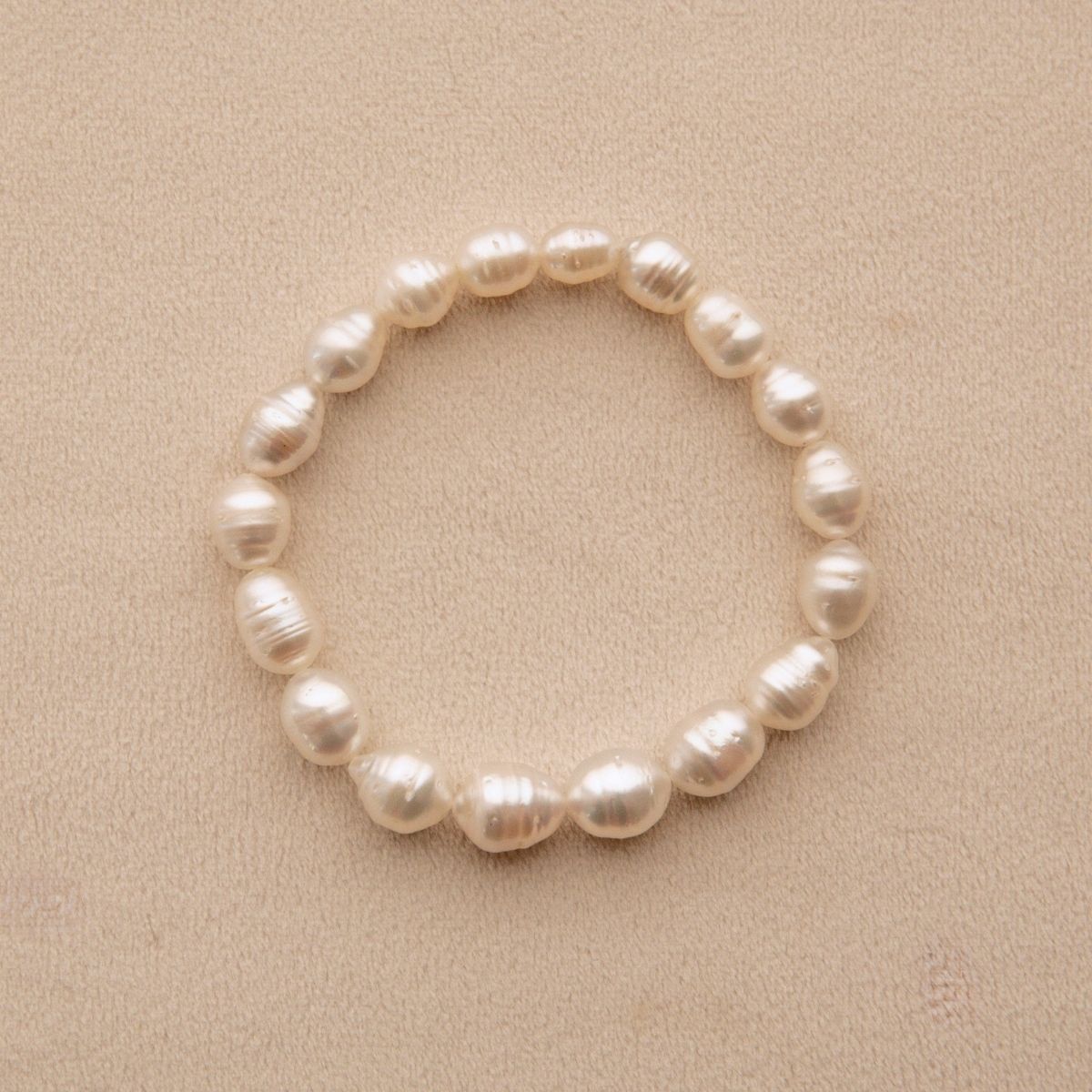 An elasticated pearl strand bracelet made of circle shape Australian Suth Sea pearls, displayed on a textured beige background.