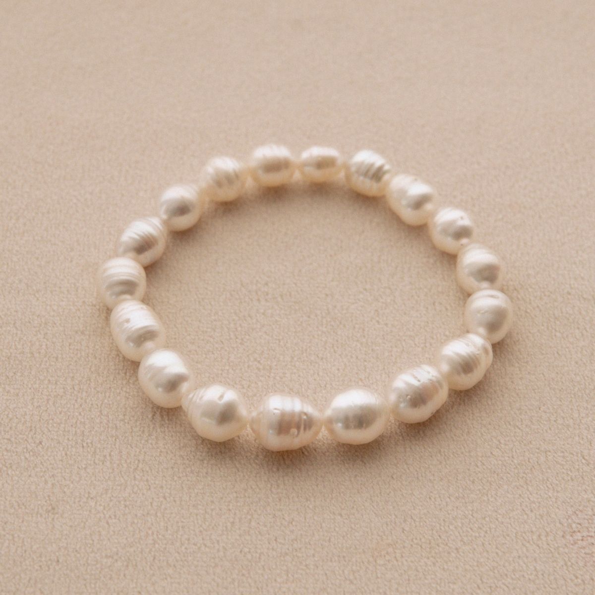A strand bracelet made of circle shape Australian South Sea pearls, displayed on a textured beige background.