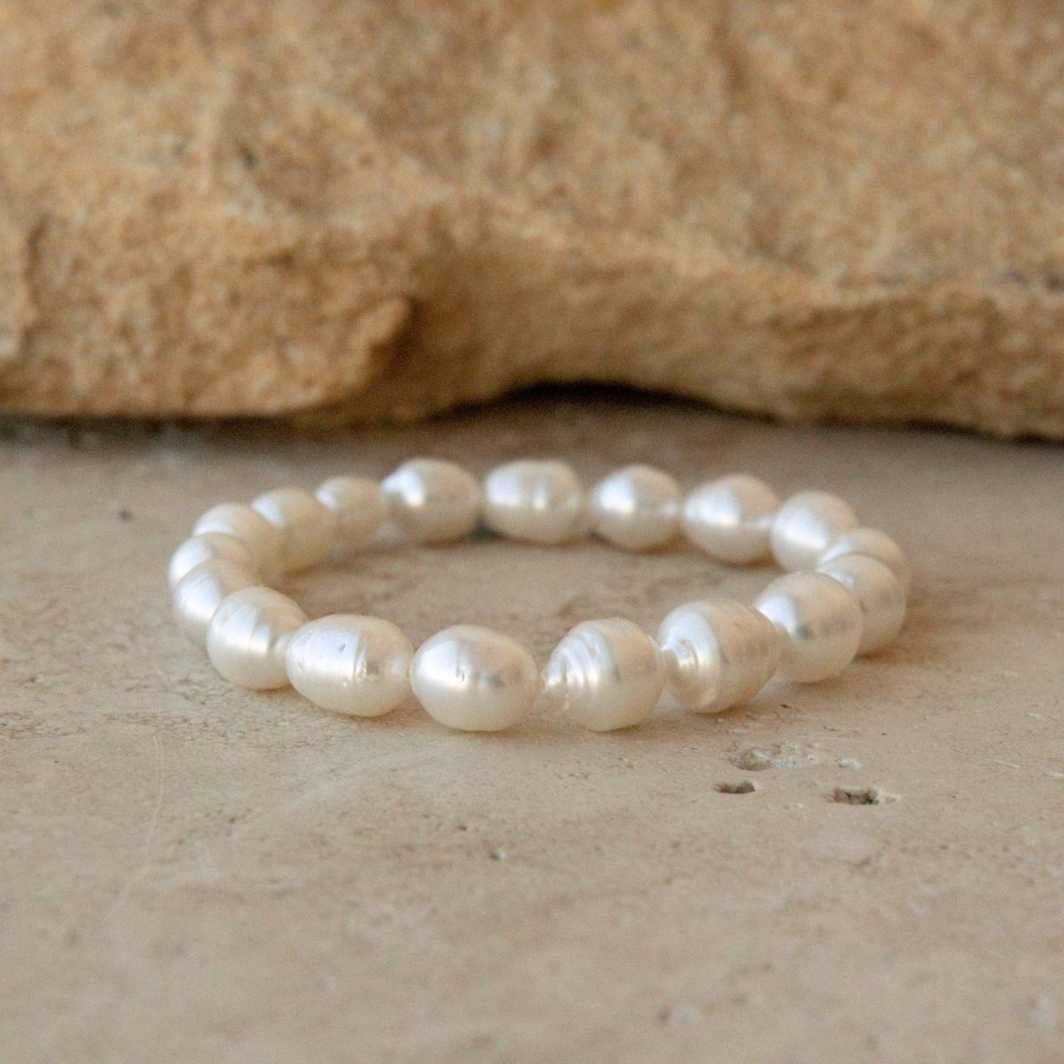 A strand bracelet made of Australian South Sea pearls, displayed on a textured beige stone surface with a larger rock in the background.