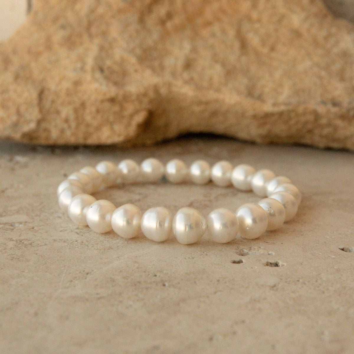 An elasticated pearl strand bracelet made of Australian South Sea pearls, displayed on a textured beige stone surface with a larger rock in the background.