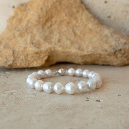 A strand bracelet made of white Australian South Sea pearls, displayed on a textured beige stone surface with a larger rock in the background.