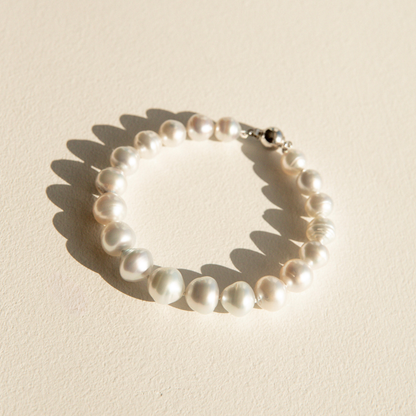 A strand bracelet made of irregular white Australian South Sea pearls with a silver-toned clasp, photographed on a warm off-white textured surface with a soft shadow.