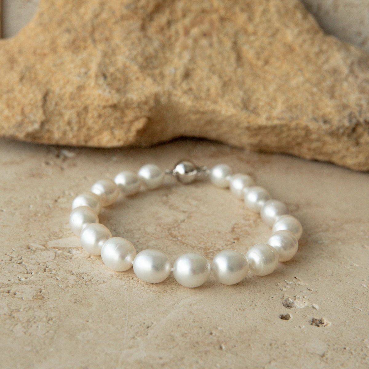 Pearl strand bracelet on a sandy surface with a rock in the background