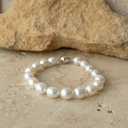 Pearl strand bracelet on a sandy surface with a rock in the background