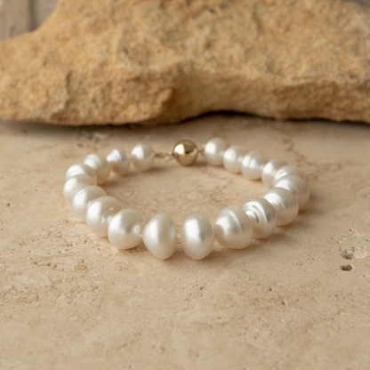 Pearl strand bracelet with a gold clasp on a beige stone surface