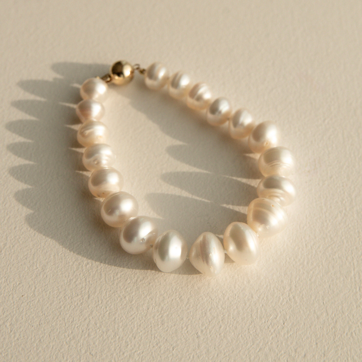 Pearl strand bracelet with a gold clasp on a beige background