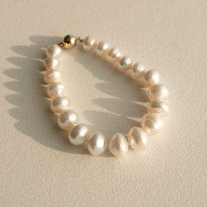 Pearl strand bracelet with a gold clasp on a beige background