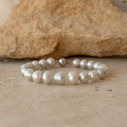 A pearl strand bracelet made of irregular white Australian South sea pearls with a 9ct white gold ball clasp, resting on a textured beige stone surface with a larger tan rock in the background.