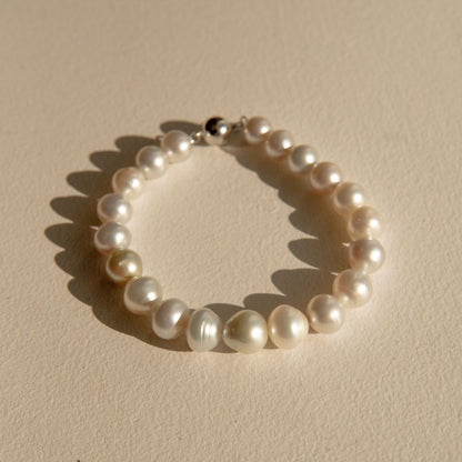 A Saltwater pearl strand bracelet with a 9ct white gold ball clasp, arranged in a circle on a textured beige surface with soft shadows.