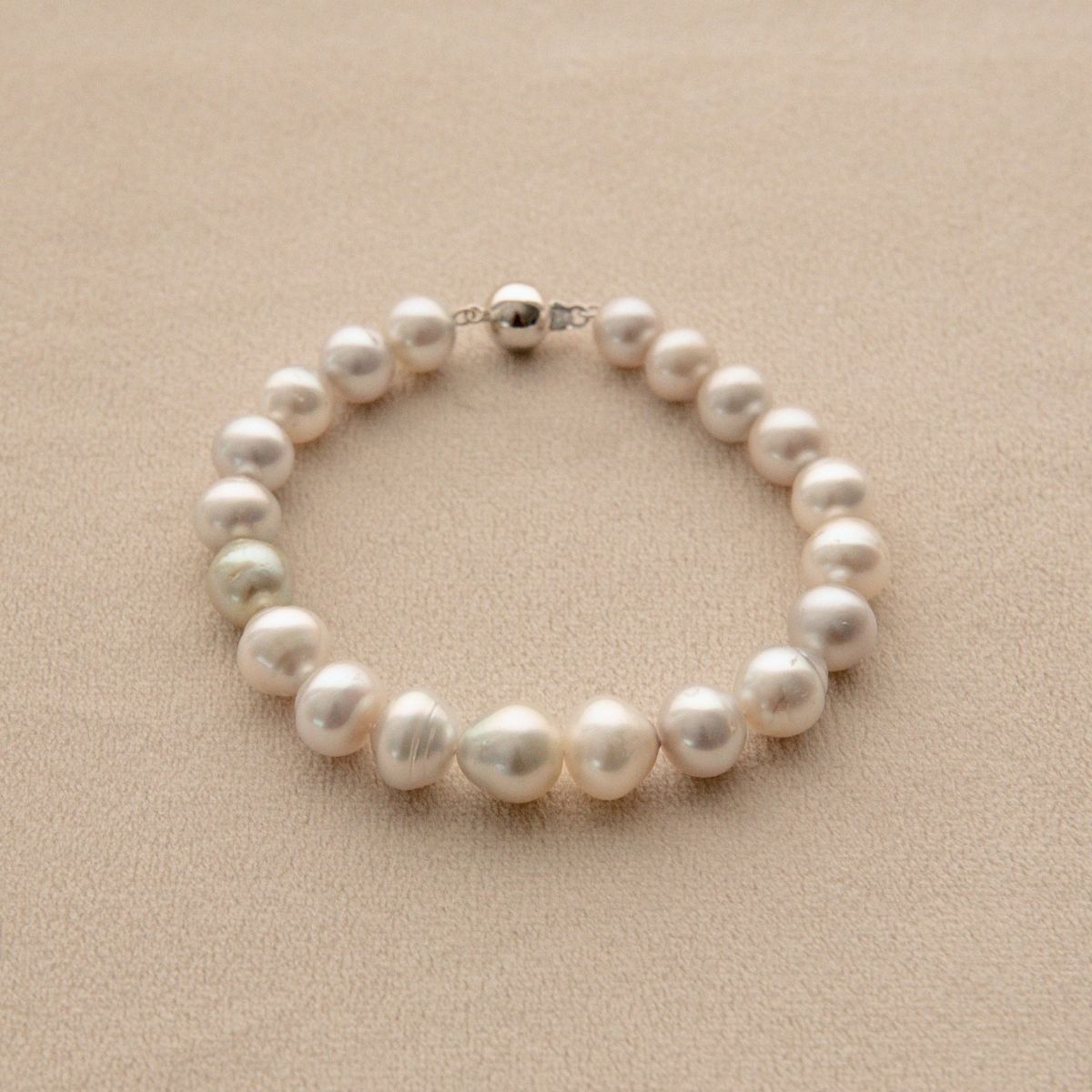 An Australian South Sea pearl bracelet with irregular circle and button shape pearls and a white gold clasp, displayed on a textured beige surface.