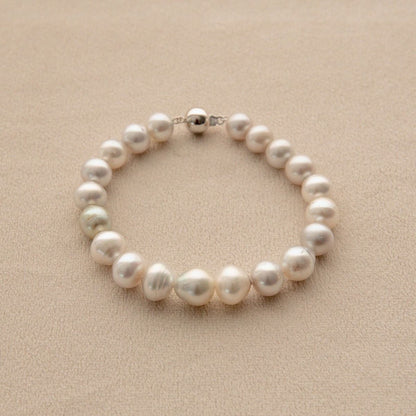 An Australian South Sea pearl bracelet with irregular circle and button shape pearls and a white gold clasp, displayed on a textured beige surface.