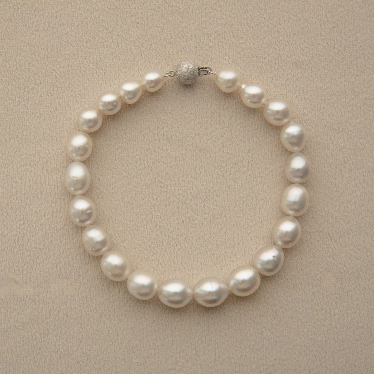 An Australian South Sea pearl strand necklace arranged in a circle on a textured beige background, featuring a silver-toned bead clasp.