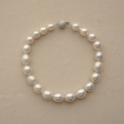 An Australian South Sea pearl strand necklace arranged in a circle on a textured beige background, featuring a silver-toned bead clasp.