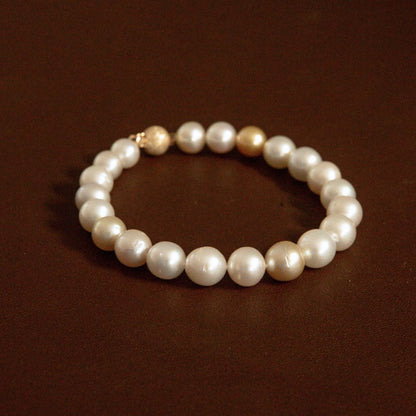 An Australian South Sea pearl strand bracelet with mostly white pearls and one prominent gold-toned pearl, displayed on a dark brown background.