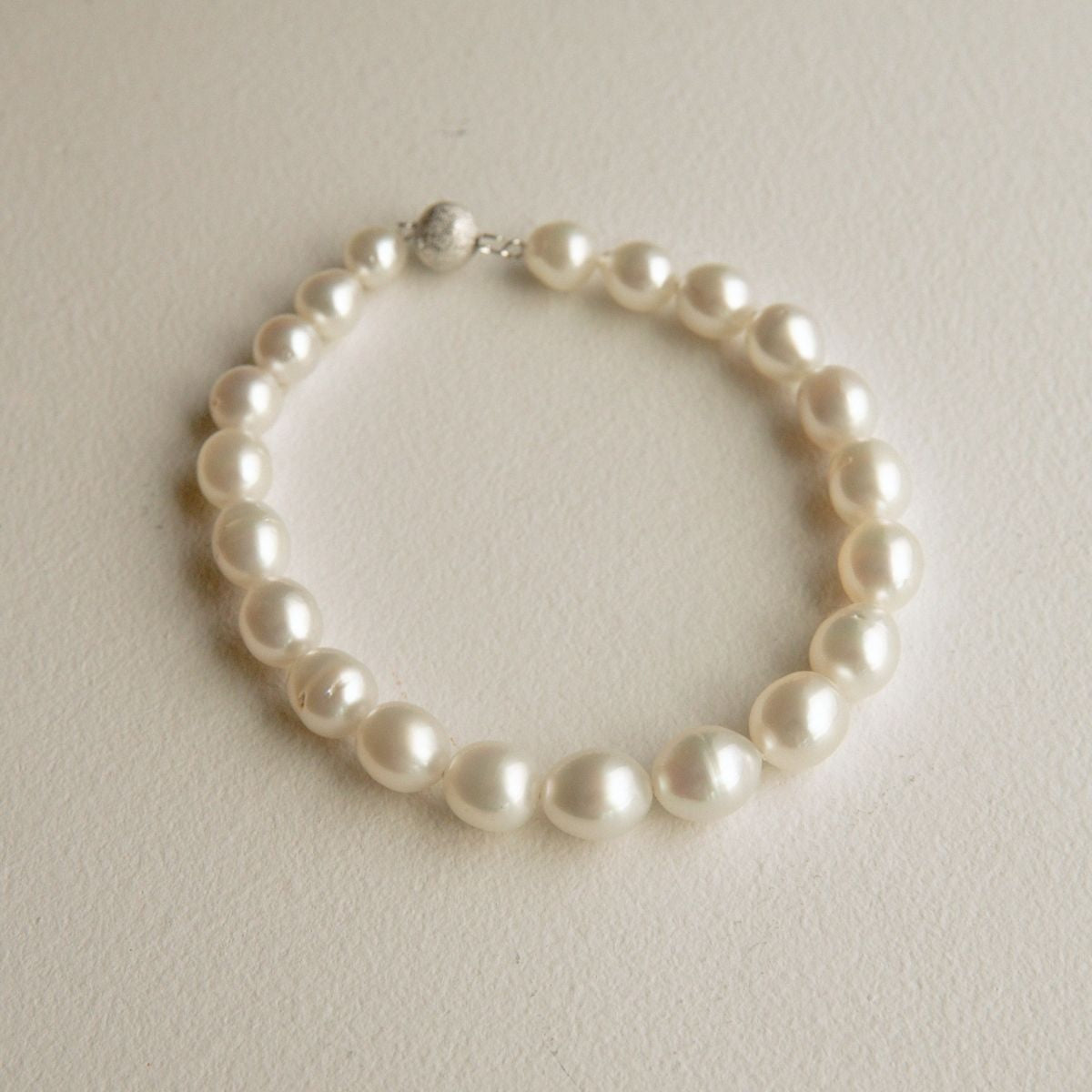 A classic pearl strand bracelet with a 9ct white gold clasp, displayed on a textured off-white surface.