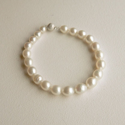 A classic pearl strand bracelet with a 9ct white gold clasp, displayed on a textured off-white surface.