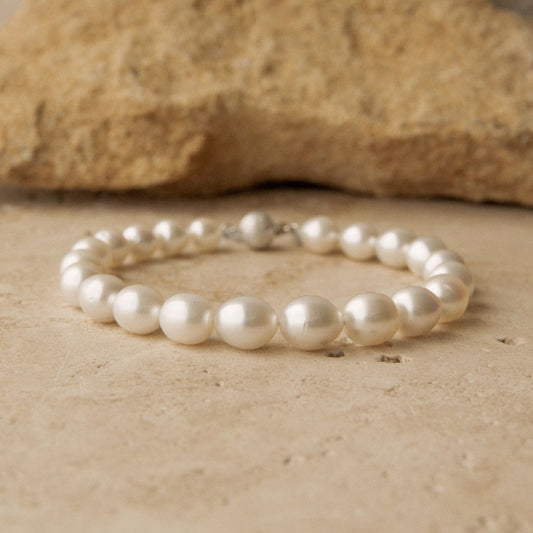 A single-strand pearl bracelet with a 9ct white gold, resting on a textured beige stone surface with a larger rock in the background.