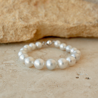 A pearl strand bracelet made of round white Australian South Sea pearls with a silver clasp, resting on a textured beige stone surface with a larger stone in the background.