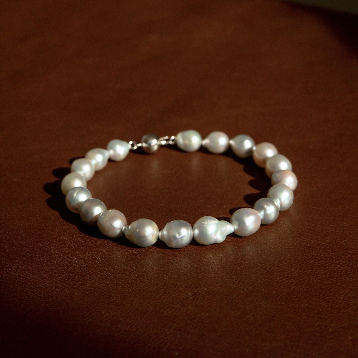 A strand bracelet made of baroque Australian Akoya pearls with an 18ct white gold clasp, resting on a dark brown leather surface.