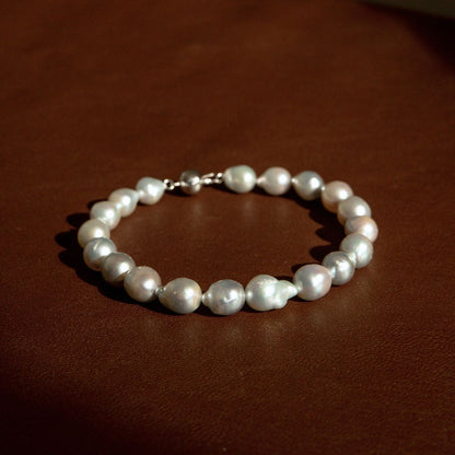 A strand bracelet made of baroque Australian Akoya pearls with an 18ct white gold clasp, resting on a dark brown leather surface.