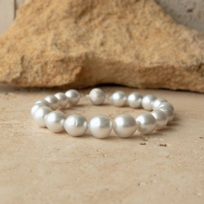 An Australian South Sea bracelet made of large, lustrous white Saltwater pearls, displayed on a textured beige stone surface with a larger rock in the background.