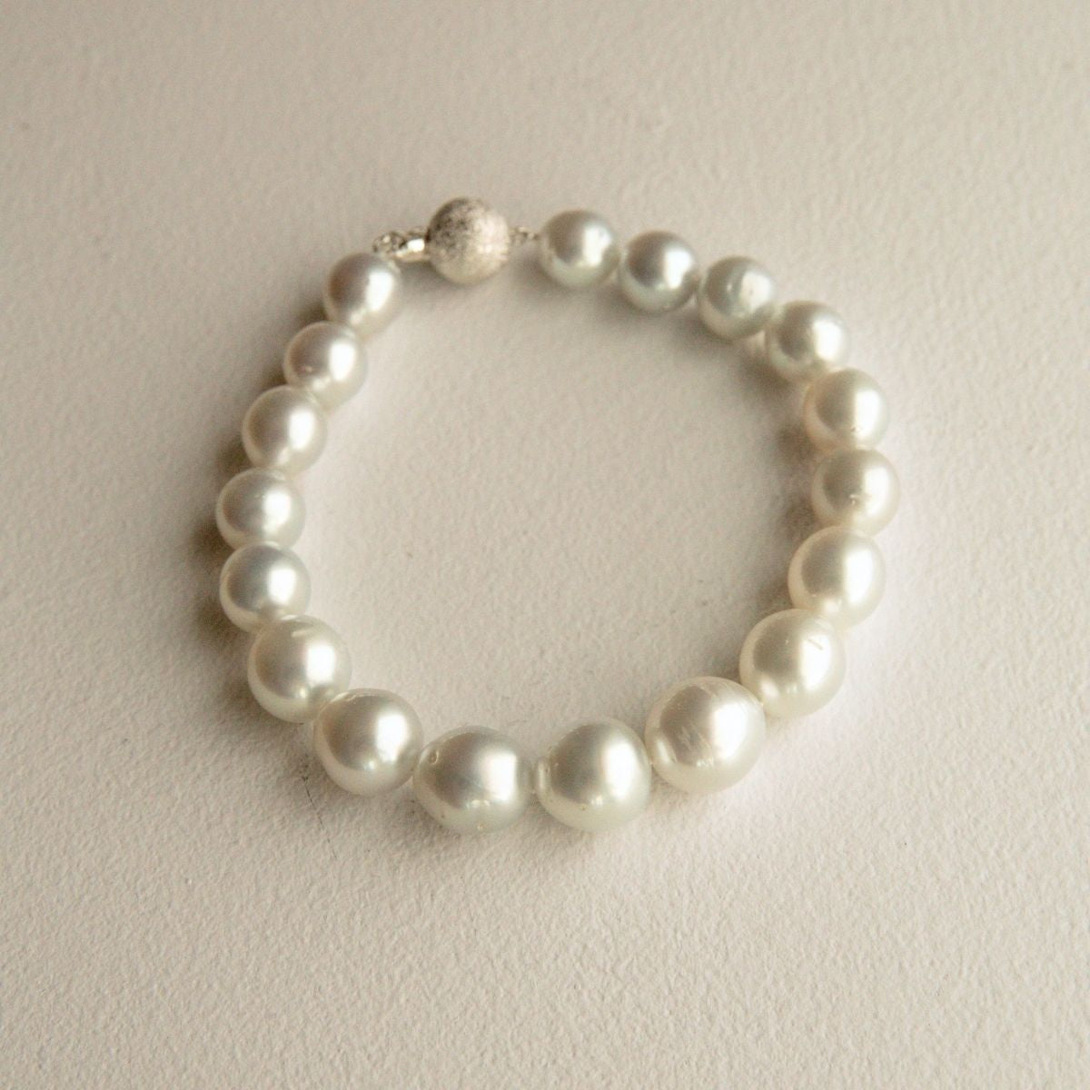 A pearl strand bracelet with a textured 9ct white gold clasp, displayed on a neutral beige background.