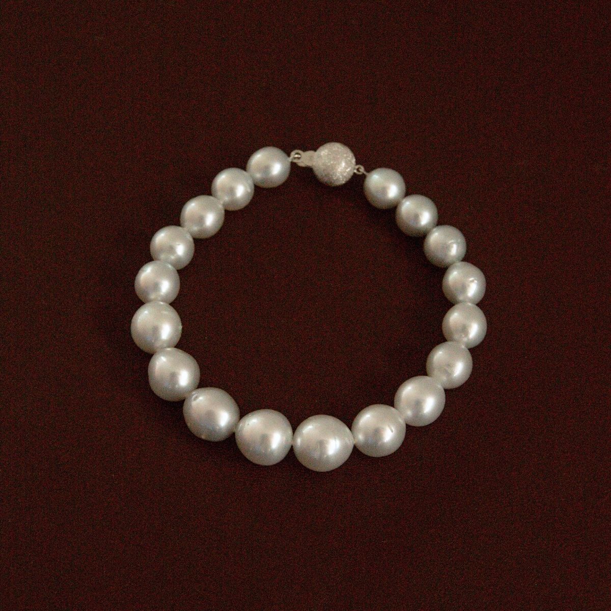 A classic Australian South Sea pearl strand bracelet with a textured 9ct white gold clasp, displayed on a dark reddish-brown background.