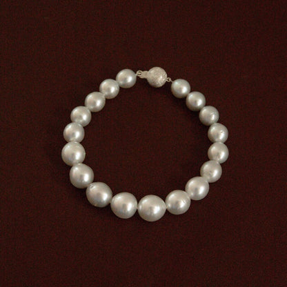 A classic Australian South Sea pearl strand bracelet with a textured 9ct white gold clasp, displayed on a dark reddish-brown background.