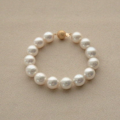 An Australian South Sea pearl strand bracelet with a textured 9ct yellow gold clasp, displayed on a neutral beige textured background.