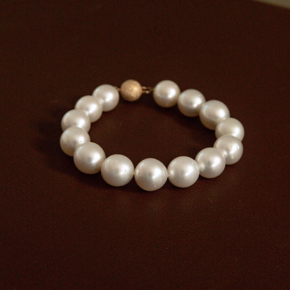 A pearl strand bracelet with a textured 9ct yellow gold, displayed on a dark brown surface.