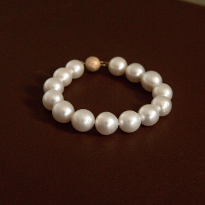 A pearl strand bracelet with a textured 9ct yellow gold, displayed on a dark brown surface.