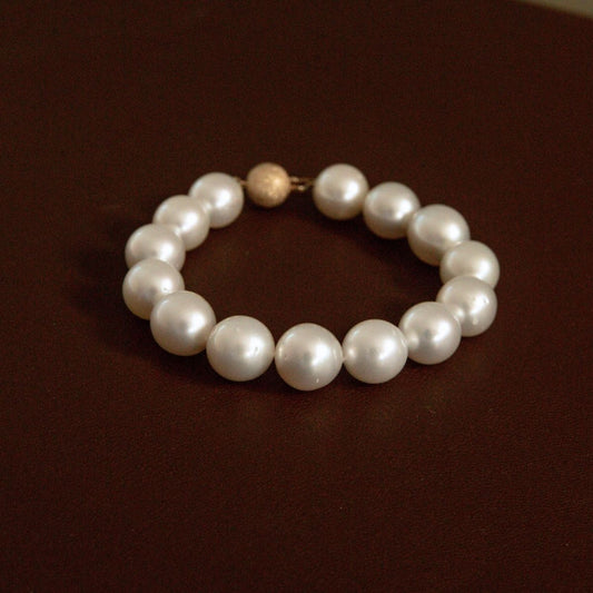 A pearl strand bracelet with a textured 9ct yellow gold, displayed on a dark brown surface.