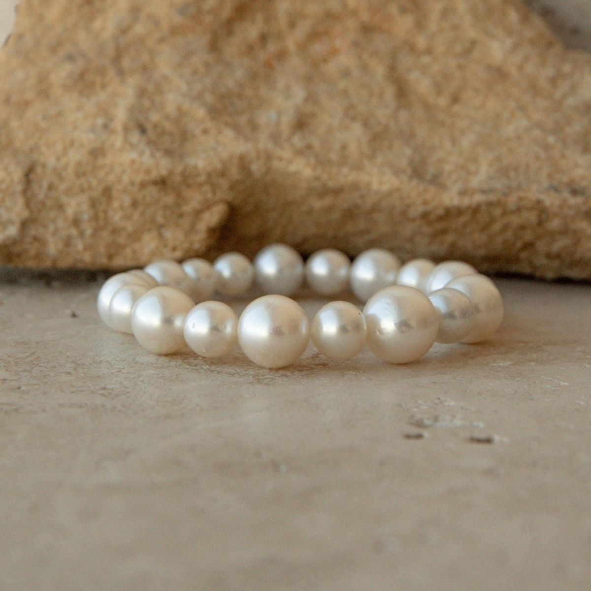 An Australian South Sea pearl strand bracelet made of large, lustrous white Saltwater pearls, displayed on a neutral stone surface with a larger textured stone in the background.