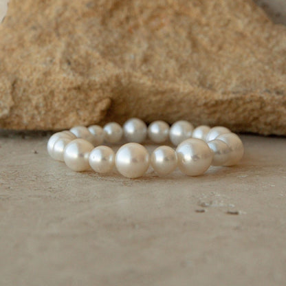 An Australian South Sea pearl strand bracelet made of large, lustrous white Saltwater pearls, displayed on a neutral stone surface with a larger textured stone in the background.