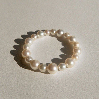 A stretch pearl strand bracelet made of large, lustrous white Australian South Sea pearls, photographed on a textured beige surface with a soft shadow.