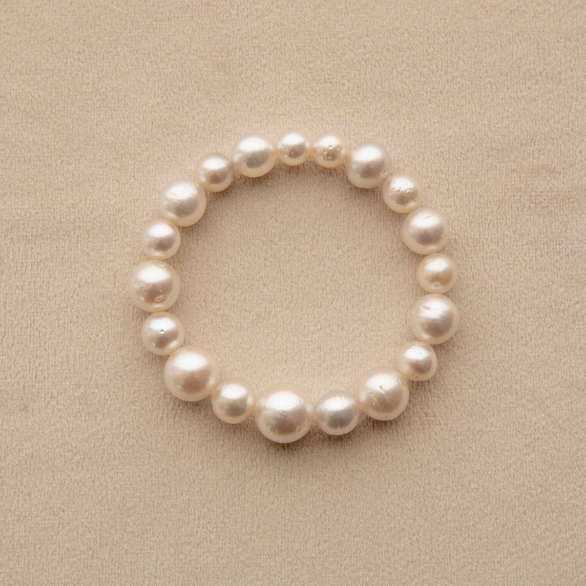 A South Sea pearl strand bracelet made of irregular white Saltwater pearls, arranged in a circle on a textured beige background.