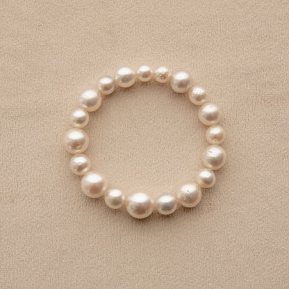 A South Sea pearl strand bracelet made of irregular white Saltwater pearls, arranged in a circle on a textured beige background.