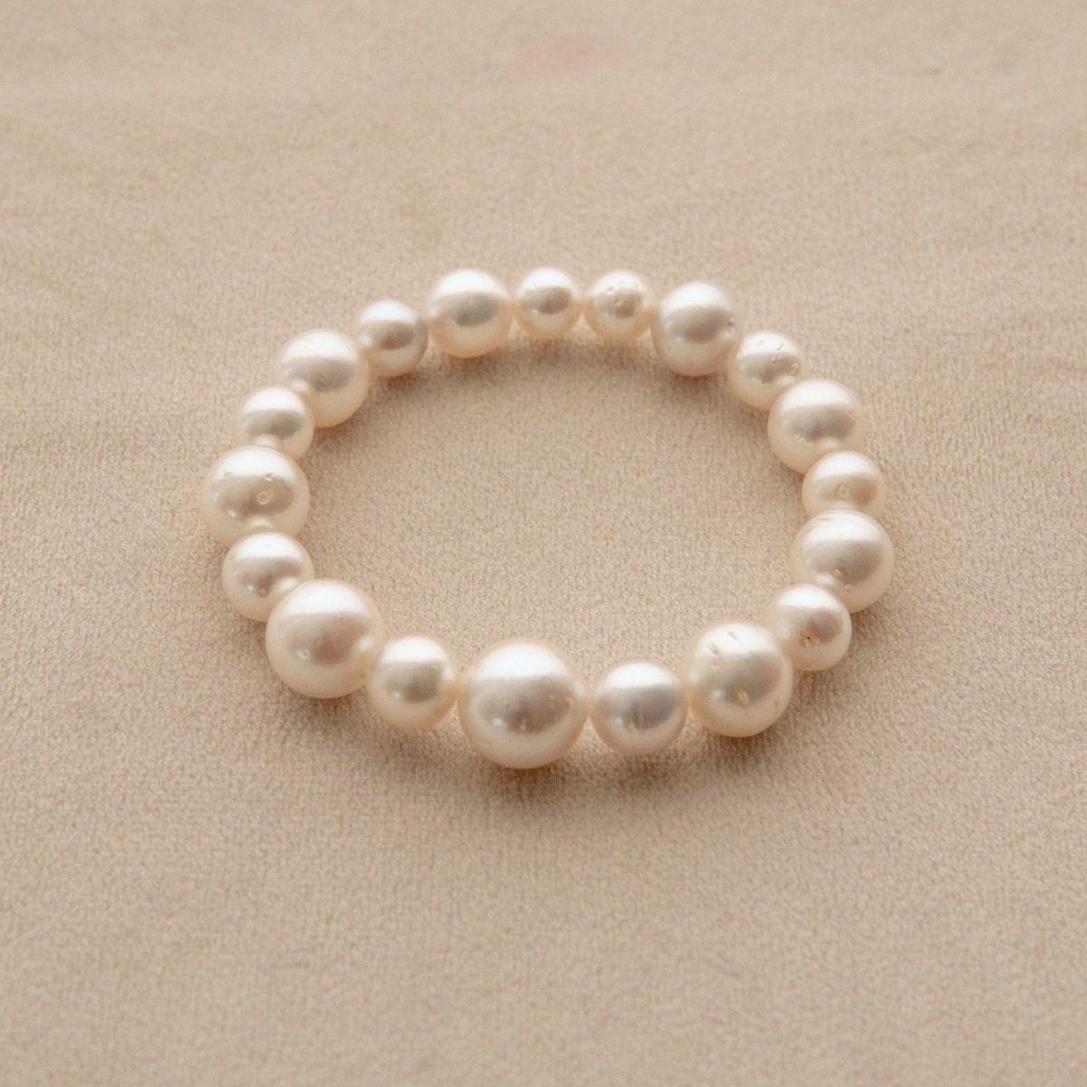 An elasticated pearl strand bracelet made of Australian South Sea pearls, displayed on a textured beige surface.