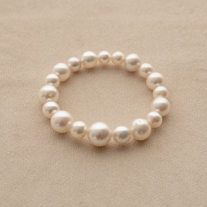 An elasticated pearl strand bracelet made of Australian South Sea pearls, displayed on a textured beige surface.