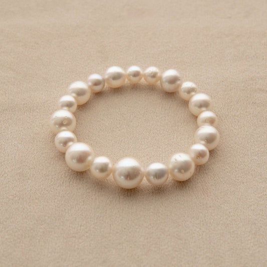 An elasticated pearl strand bracelet made of Australian South Sea pearls, displayed on a textured beige surface.
