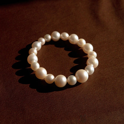 A pearl strand bracelet made of large, lustrous white Cygnet Bay grown Australian South Sea pearls, arranged in a circle on a dark brown textured leather background.