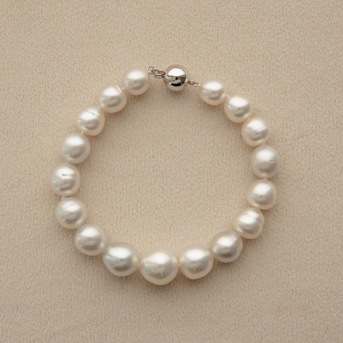 A Saltwater pearl bracelet with irregular white Australian South Sea pearls grown at Cygnet Bay Pearl Farm and a 9ct white gold clasp, displayed on a textured beige background.