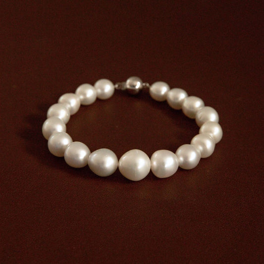 An Australian South Sea pearl bracelet with irregular white pearls and a 9ct white gold ball clasp, displayed on a dark brown background.