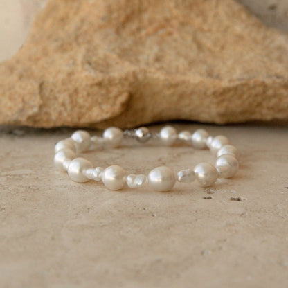 A Keshi and South Sea pearl strand bracelet, displayed on a textured stone surface with a blurred tan rock in the background.