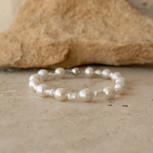 A Keshi and South Sea pearl strand bracelet, displayed on a textured stone surface with a blurred tan rock in the background.