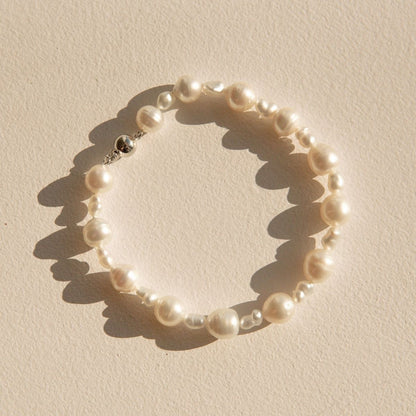 A pearl strand bracelet made of irregular Keshi and South Sea pearls, arranged in a circle on a textured beige surface with hard sunlight casting shadows.