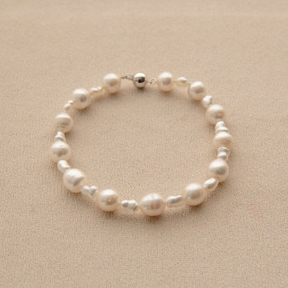 A pearl bracelet with mixed sizes of white Keshi and South Sea pearls, displayed on a textured beige surface.