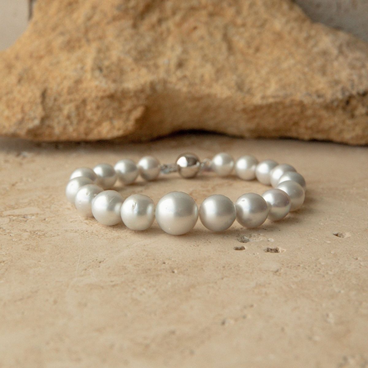 An Australian South Sea pearl strand bracelet with a 9ct white gold clasp, displayed on a textured beige stone surface with a larger rock in the background.